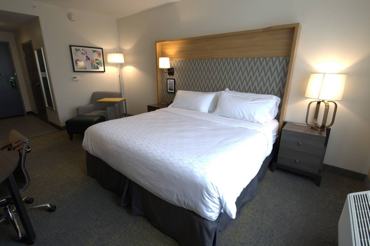 A hotel room with a large bed, a desk, a chair, and two bedside tables with lamps.