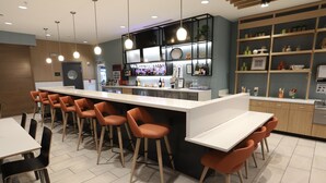 A modern bar area with a long counter, orange bar stools, and a variety of bottles and glasses. - Holiday Inn Hotel & Suites Hopkinsville - Convention Ctr by IHG (Hopkinsville)