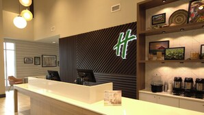 A reception desk with a modern design, a large logo on the wall, and a coffee station with multiple coffee makers. - Holiday Inn Hotel & Suites Hopkinsville - Convention Ctr by IHG (Hopkinsville)