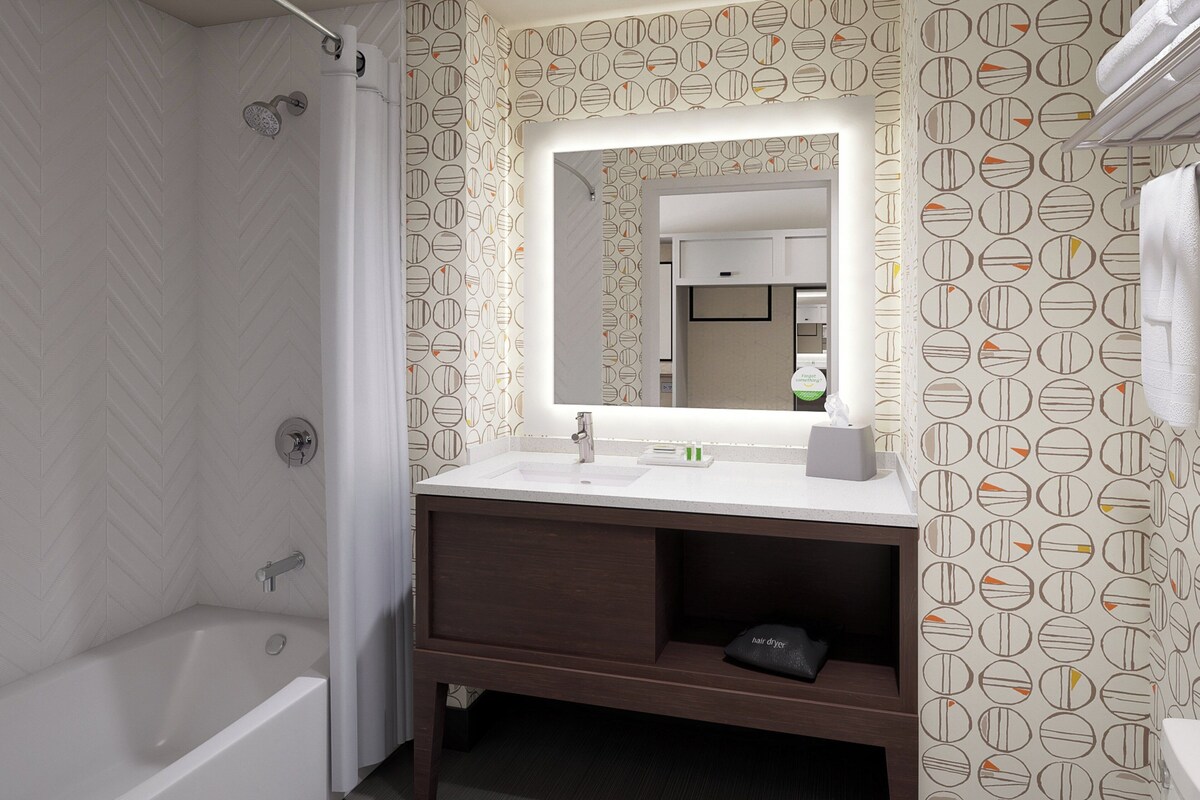 Un baño con una bañera blanca, tocador con espejo y papel tapiz estampado.