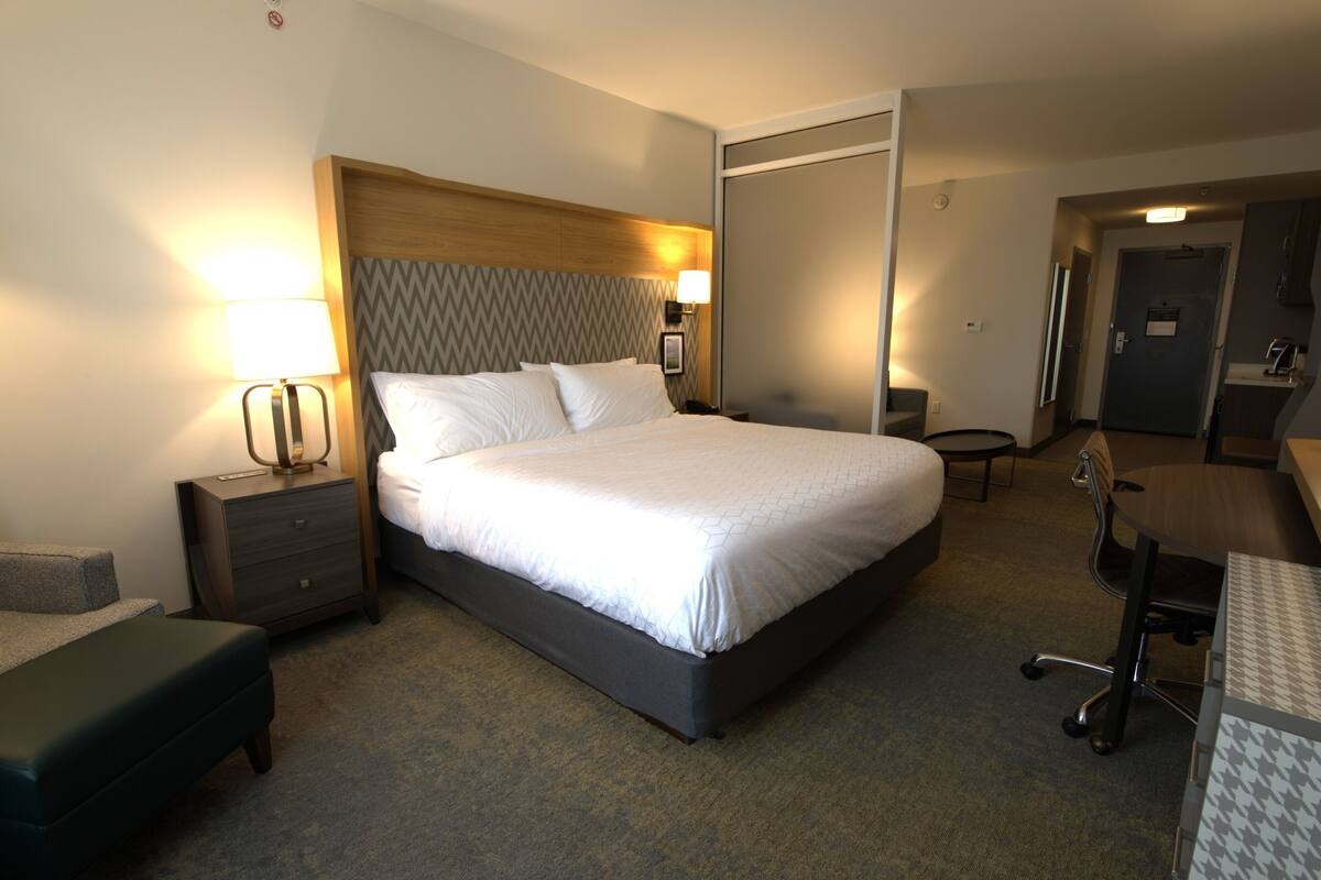 A hotel room with a bed, bedside table, lamp, desk, chair, and a wardrobe.