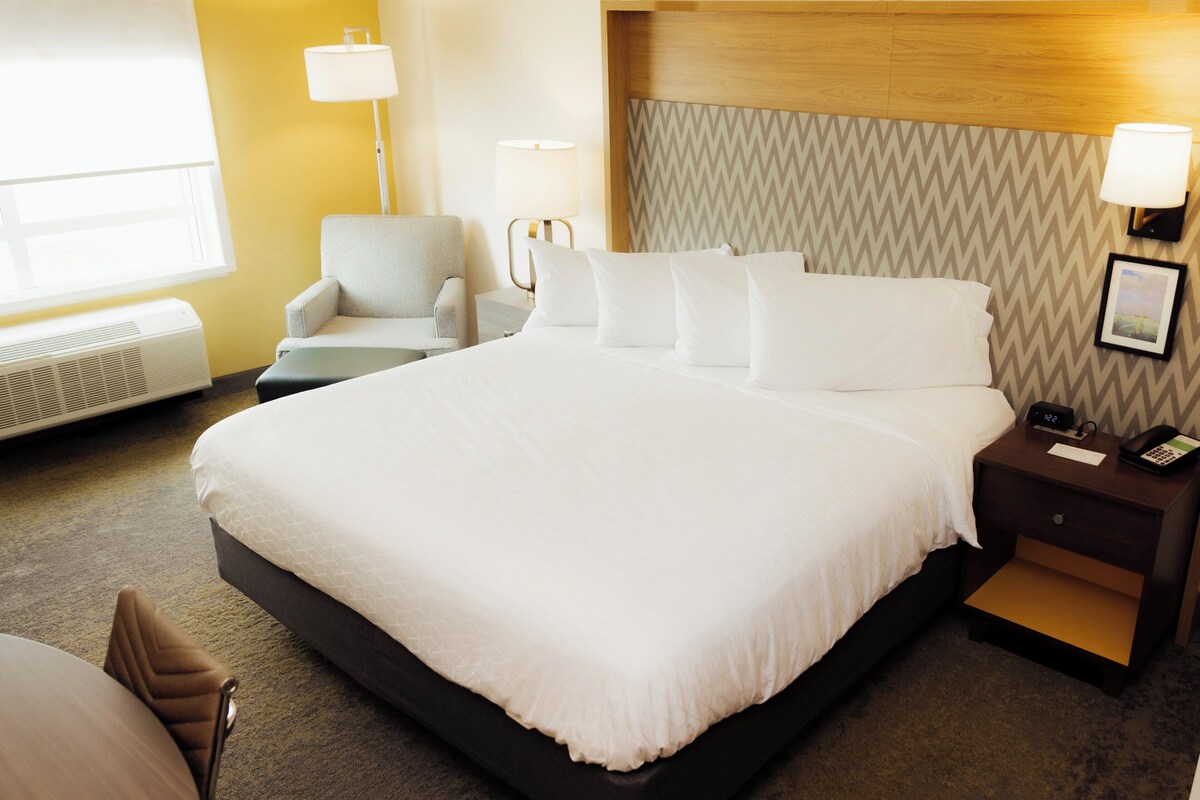 Una habitación de hotel con una cama grande, dos mesitas de noche, una silla, un escritorio y una ventana.