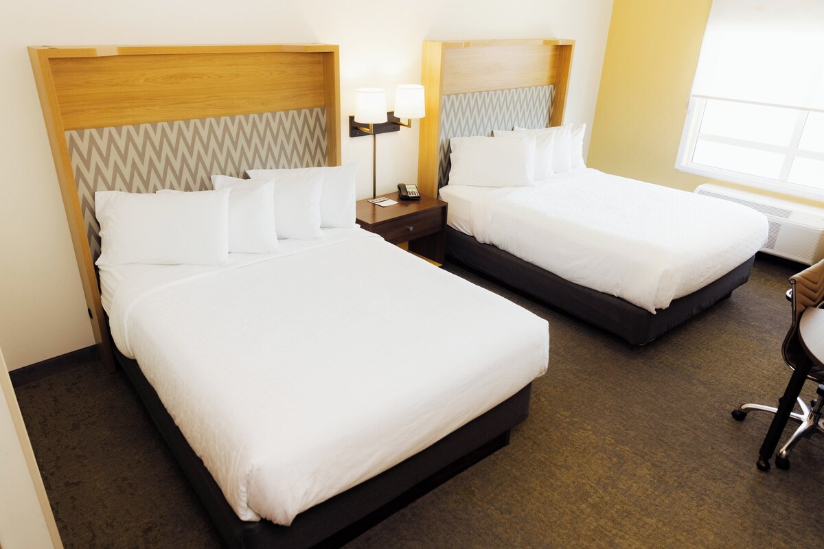 Dos camas individuales con cabeceras, mesitas de noche con lámparas y una silla en una habitación de hotel.