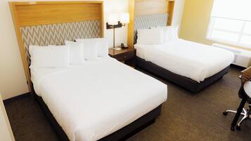 Two single beds with headboards, bedside tables with lamps, and a chair in a hotel room.