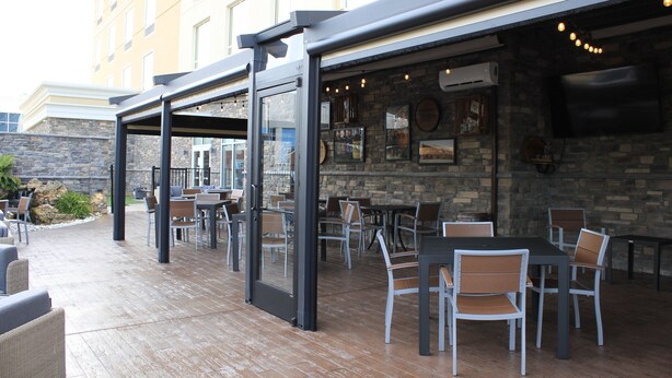 An outdoor patio area with tables and chairs, a stone wall, and a building in the background. - Holiday Inn Hotel & Suites Hopkinsville - Convention Ctr by IHG (Hopkinsville)