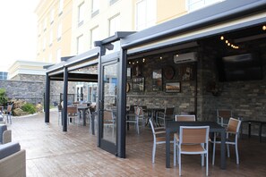 Un patio al aire libre con mesas y sillas, un muro de piedra y un edificio al fondo.