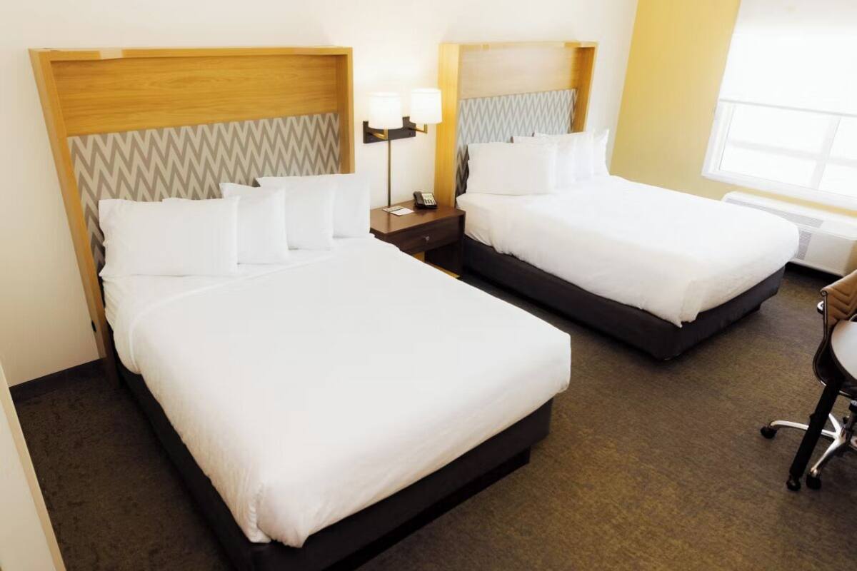 Two single beds with wooden headboards, a bedside table with a lamp, and a chair.