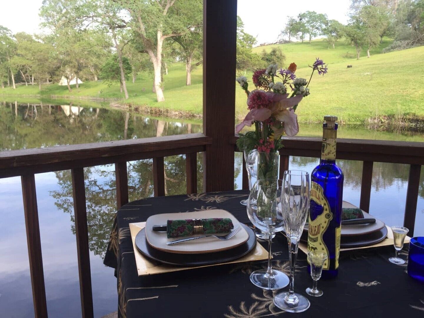 Une table dressée pour deux personnes, avec une bouteille de champagne, un vase rempli de fleurs et une vue magnifique sur un lac et des arbres.