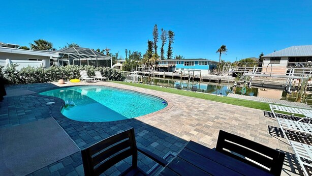 En swimmingpool med en buet kant, omgivet af en patio med stole og et bord.