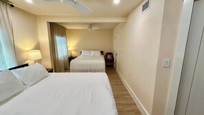 A hotel room with two beds, a ceiling fan, a nightstand, a lamp, and a chair.