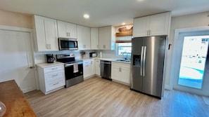 A modern kitchen with white cabinets, stainless steel appliances, and a wooden floor.