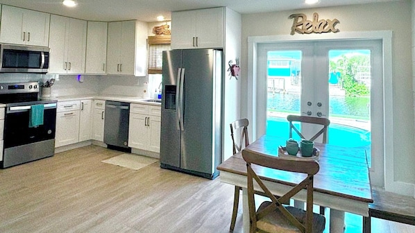 A modern kitchen with white cabinets, stainless steel appliances, and a view of a swimming pool through a glass door.