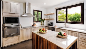 A modern kitchen with wooden cabinets, stainless steel appliances, and a large island with fresh fruit.