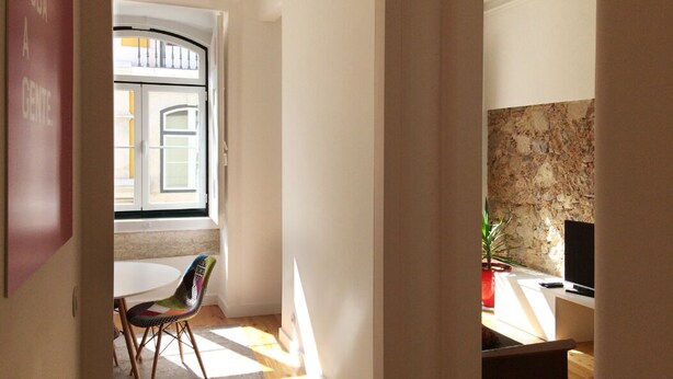 A room with a large window, a white chair, a television, and a stone wall. - Apt Traditional Charm & Modern Design in Baixa - Lisbon Historic Center (Lisboa)