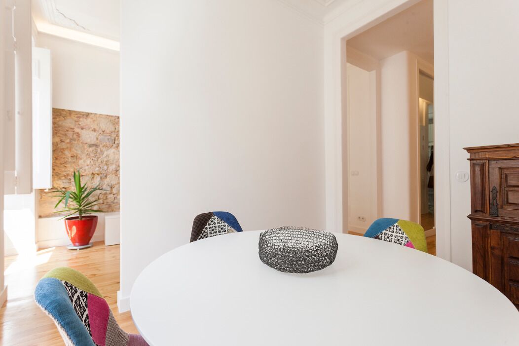 Een eetgedeelte met een ronde tafel, kleurrijke stoelen en een potplant.