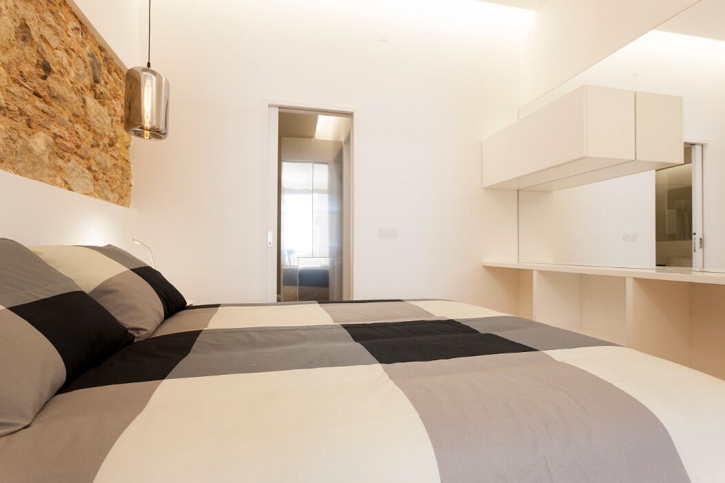 A modern bedroom with a large bed, a stone accent wall, a hanging light fixture, and a built-in wardrobe.