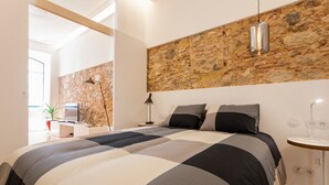 A modern bedroom with a large bed, a stone accent wall, a small bedside table, a lamp, and a TV. - Apt Traditional Charm & Modern Design in Baixa - Lisbon Historic Center (Lisboa)