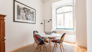 A dining area with a round table, colorful chairs, a framed black and white photo, and a window with a view of buildings. - Apt Traditional Charm & Modern Design in Baixa - Lisbon Historic Center (Lisboa)