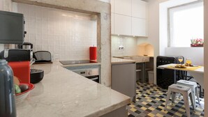 A compact kitchen with white cabinets, a marble countertop, a small dining area with a table and chairs, and a window with a view. - Apt Traditional Charm & Modern Design in Baixa - Lisbon Historic Center (Lisboa)