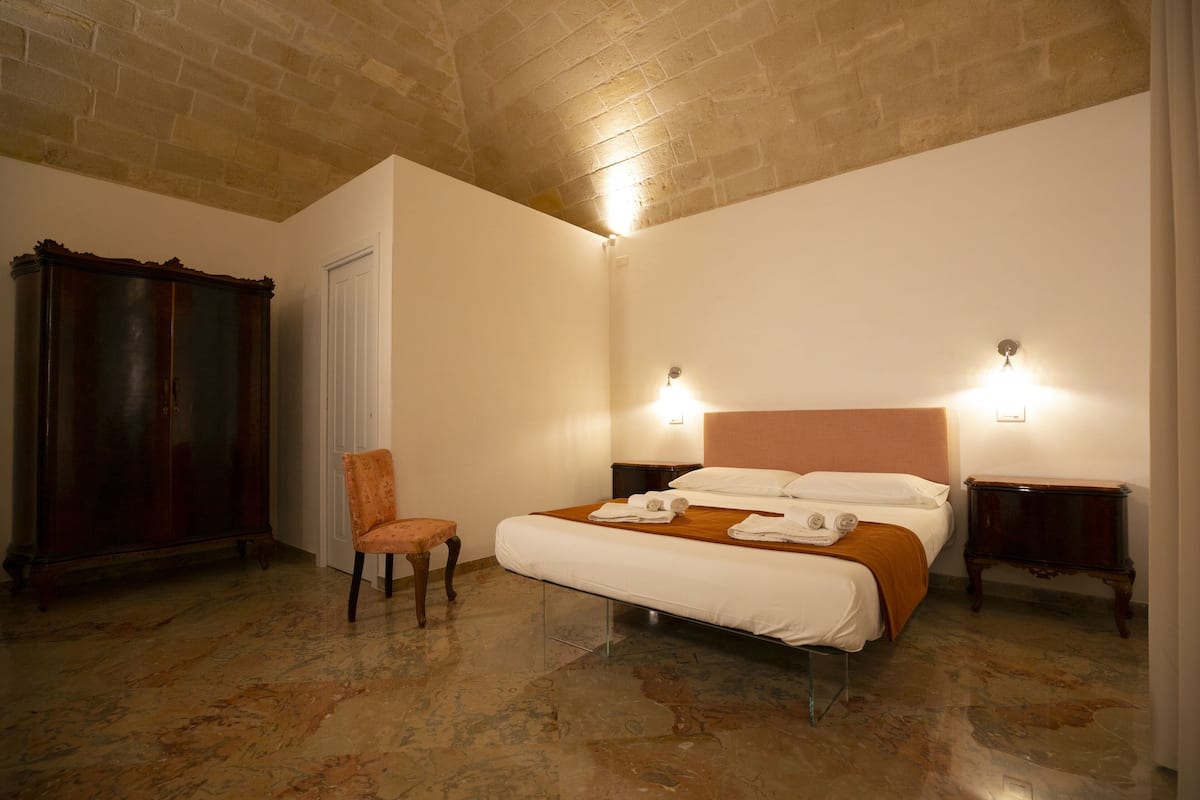A bedroom with a bed, a chair, a wardrobe, and a nightstand.