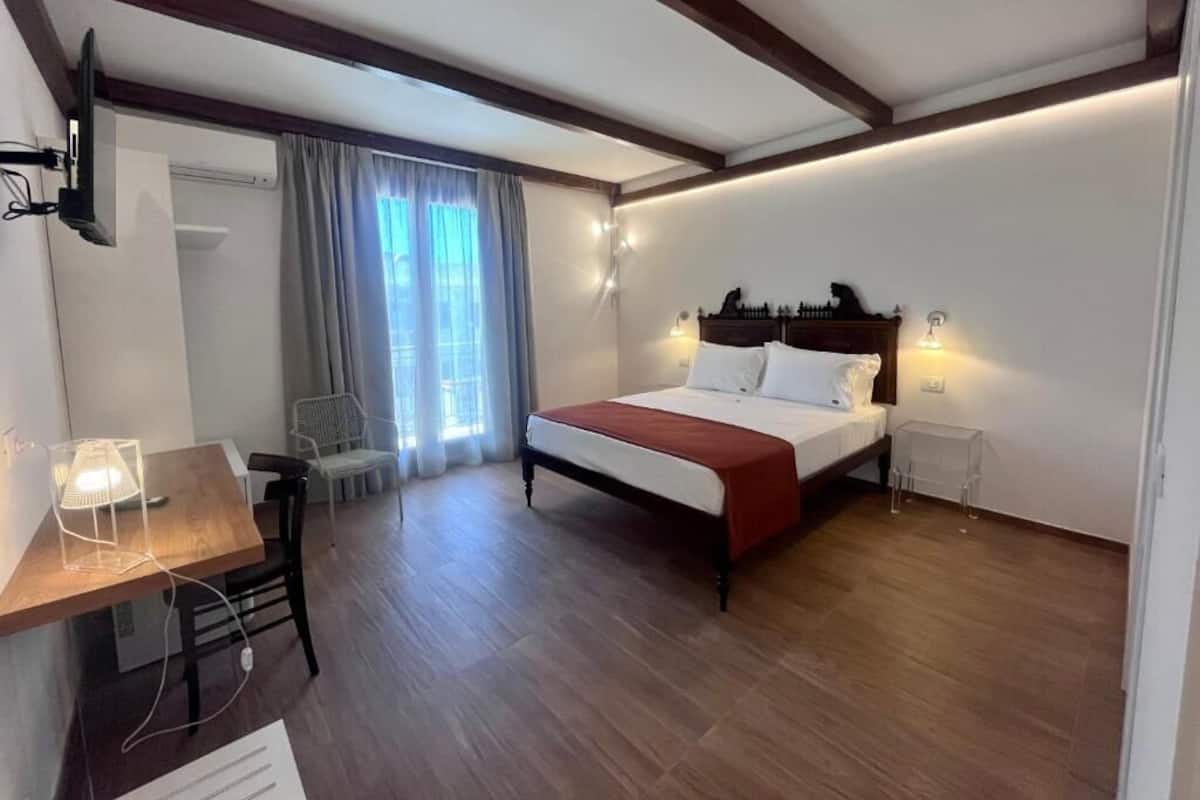 A bedroom with a wooden bed, a desk with a lamp, and a chair.