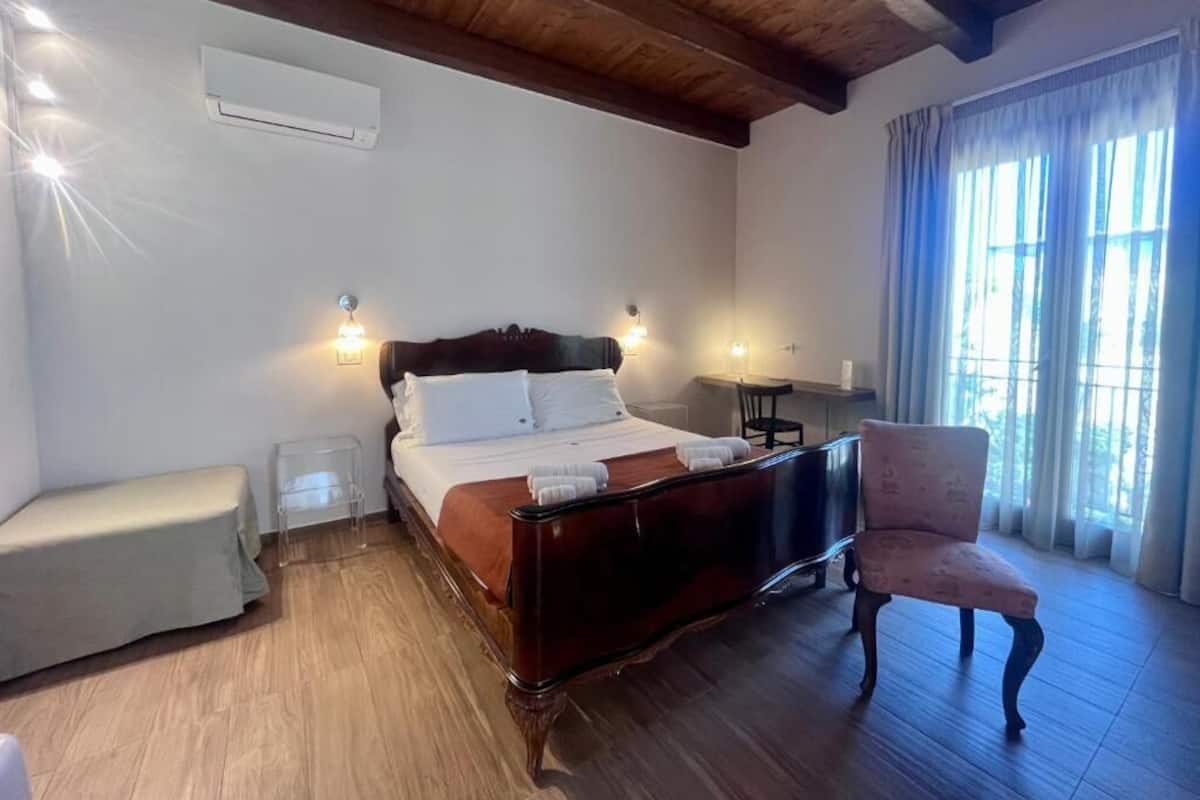 A bedroom with a wooden bed, bedside tables, a chair, and a window with curtains.