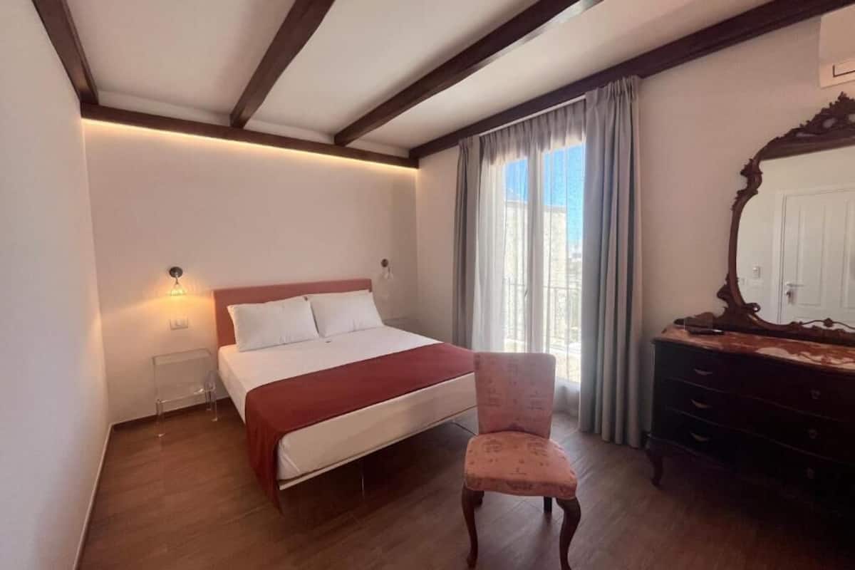 A bedroom with a bed, a chair, a dresser, and a mirror.