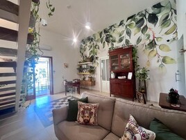 A living room with a sofa, a wooden cabinet, and a wall with a leafy pattern.