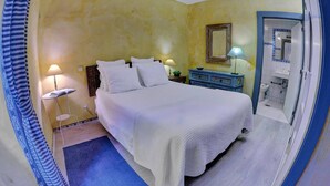 Un dormitorio con cama, lámparas de noche, cómoda, espejo y un baño visible a través de una puerta abierta.
