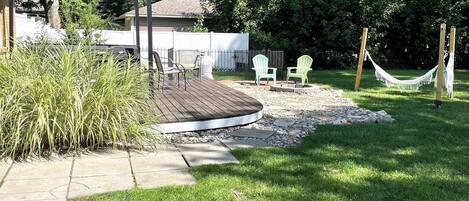 A backyard with a wooden deck, outdoor seating, and a hammock.