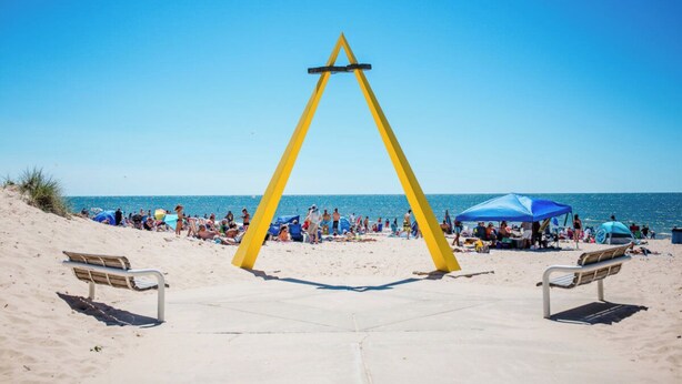 A beach with a yellow triangular structure, two benches, and people in the background. - Breezy Pad, Close to the Lake, with Hot Tub (St Joseph)