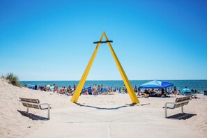 En strand med en gul, trekantet struktur, to bænke og mennesker i baggrunden.