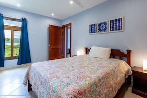 Een slaapkamer met een groot bed, een houten deur en een raam met gordijnen.
