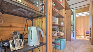 A kitchen with wooden shelves, a kettle, a phone, and various kitchen utensils.