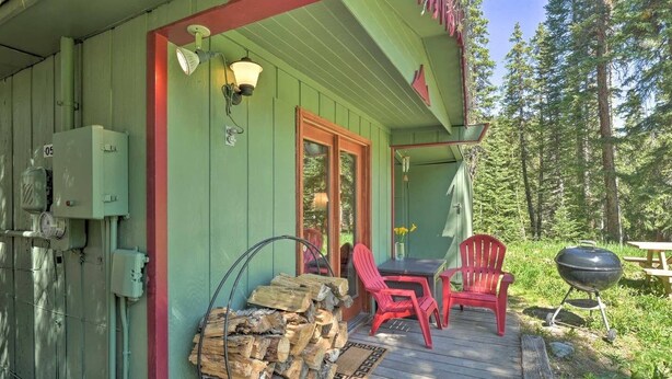 A wooden deck with a table and chairs, a grill, and a stack of firewood.