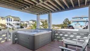Um deck coberto ao ar livre com hidromassagem, bancos de madeira e vista para casas residenciais.