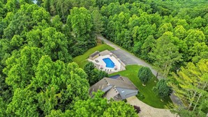 An aerial view of a residential area with a swimming pool, a house, and surrounding greenery.