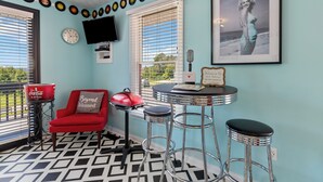 A room with a retro design, featuring a red chair, a small table with a vintage microphone, and a wall adorned with vinyl records.