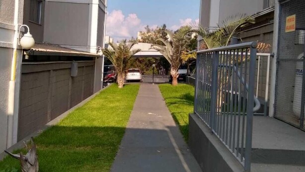 Ein Weg zwischen zwei Gebäuden mit einer Grünfläche und einem Zaun an der Seite.