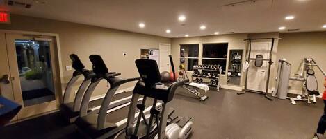 Un gimnasio con cintas de correr, máquinas de pesas y un estante con mancuernas.