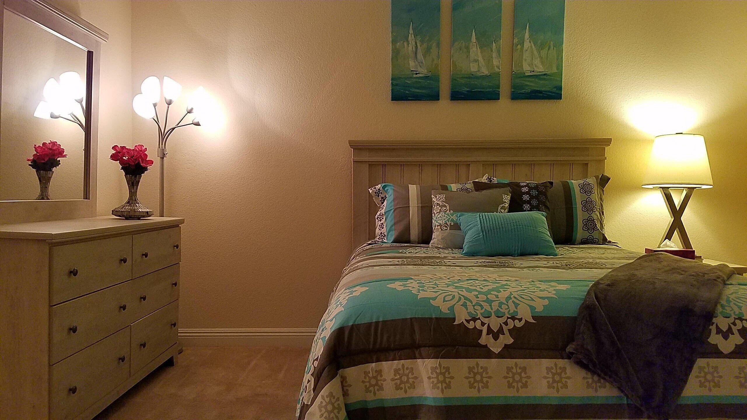 A bedroom with a bed, dresser, nightstand, and two wall-mounted lamps.