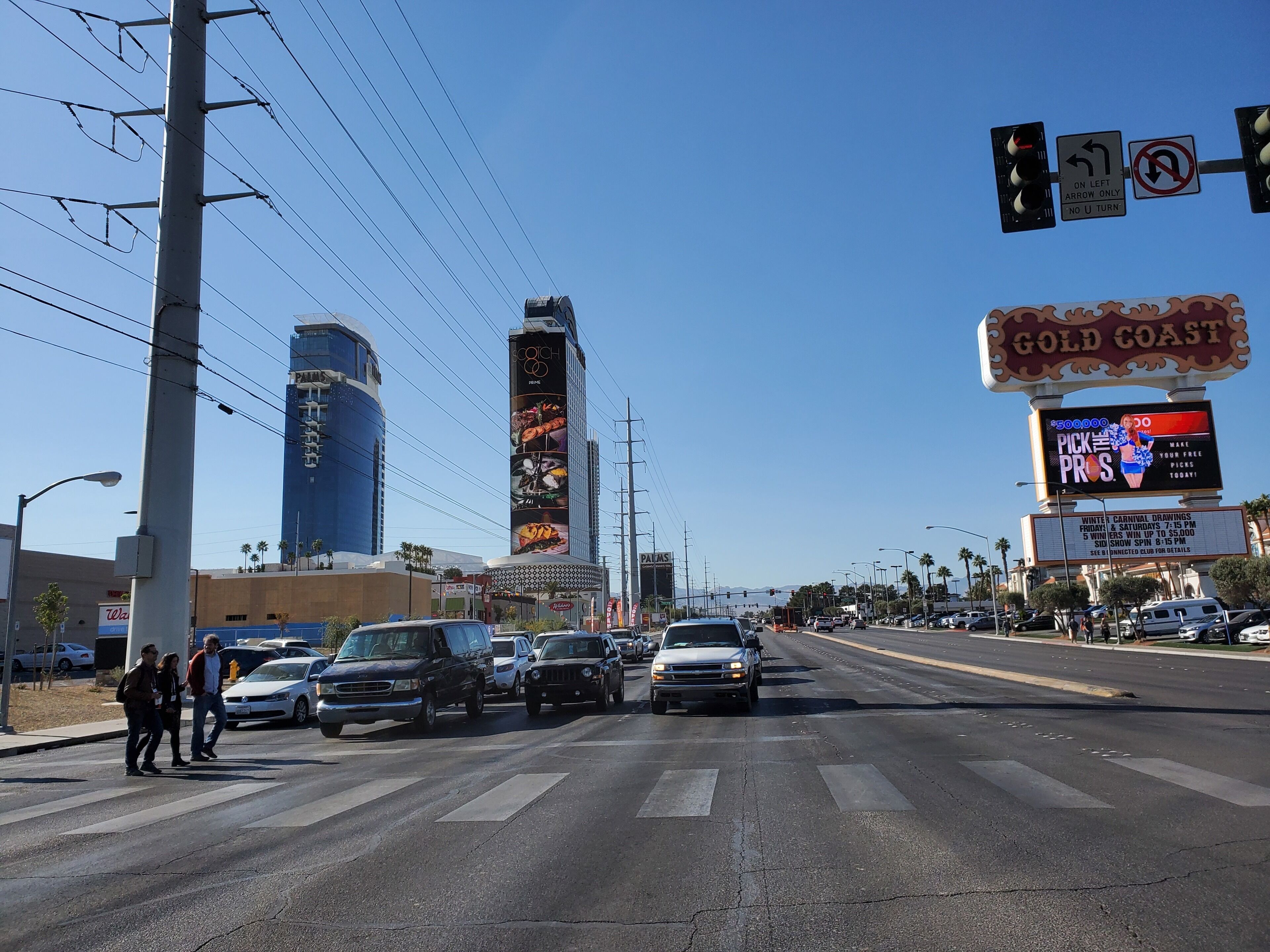 A busy street with cars, pedestrians, and a large building with a sign reading "Gold Coast".