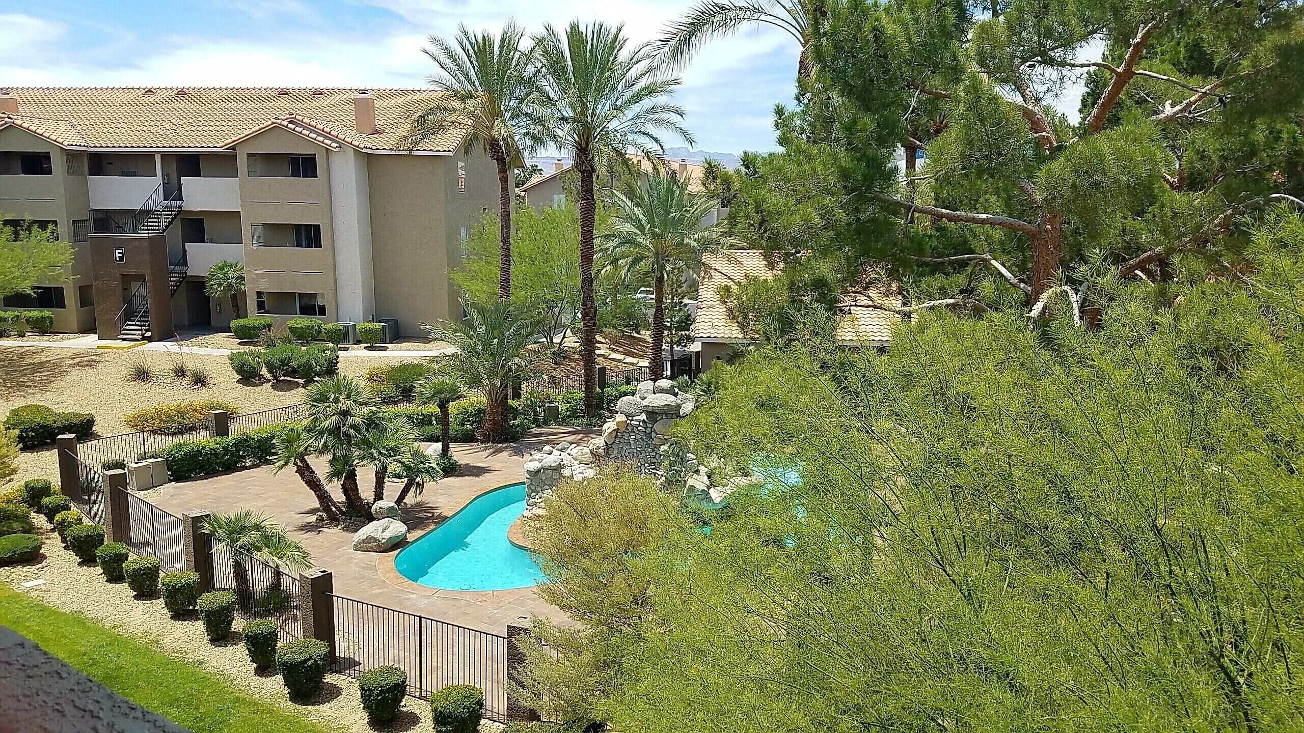 A residential building with a swimming pool surrounded by greenery and a fenced area.