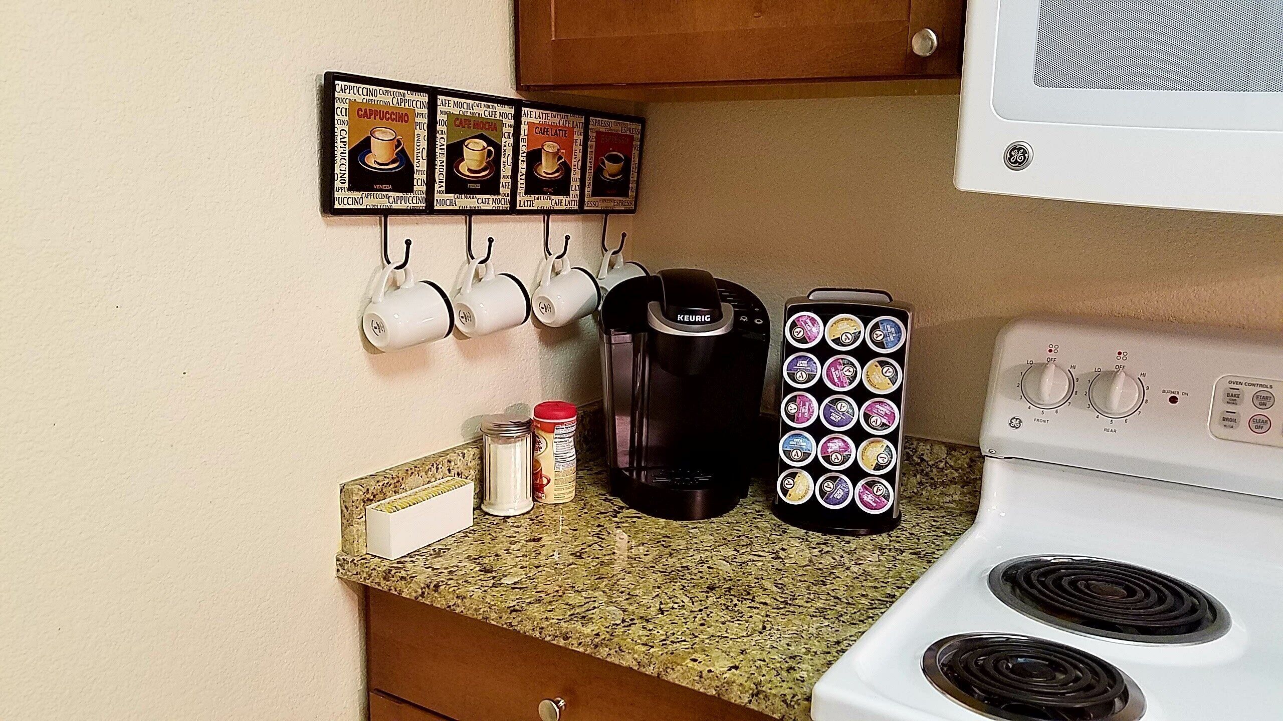 A kitchen with a GE stove, a Keurig coffee maker, a coffee pod holder, and a set of mugs on hooks.
