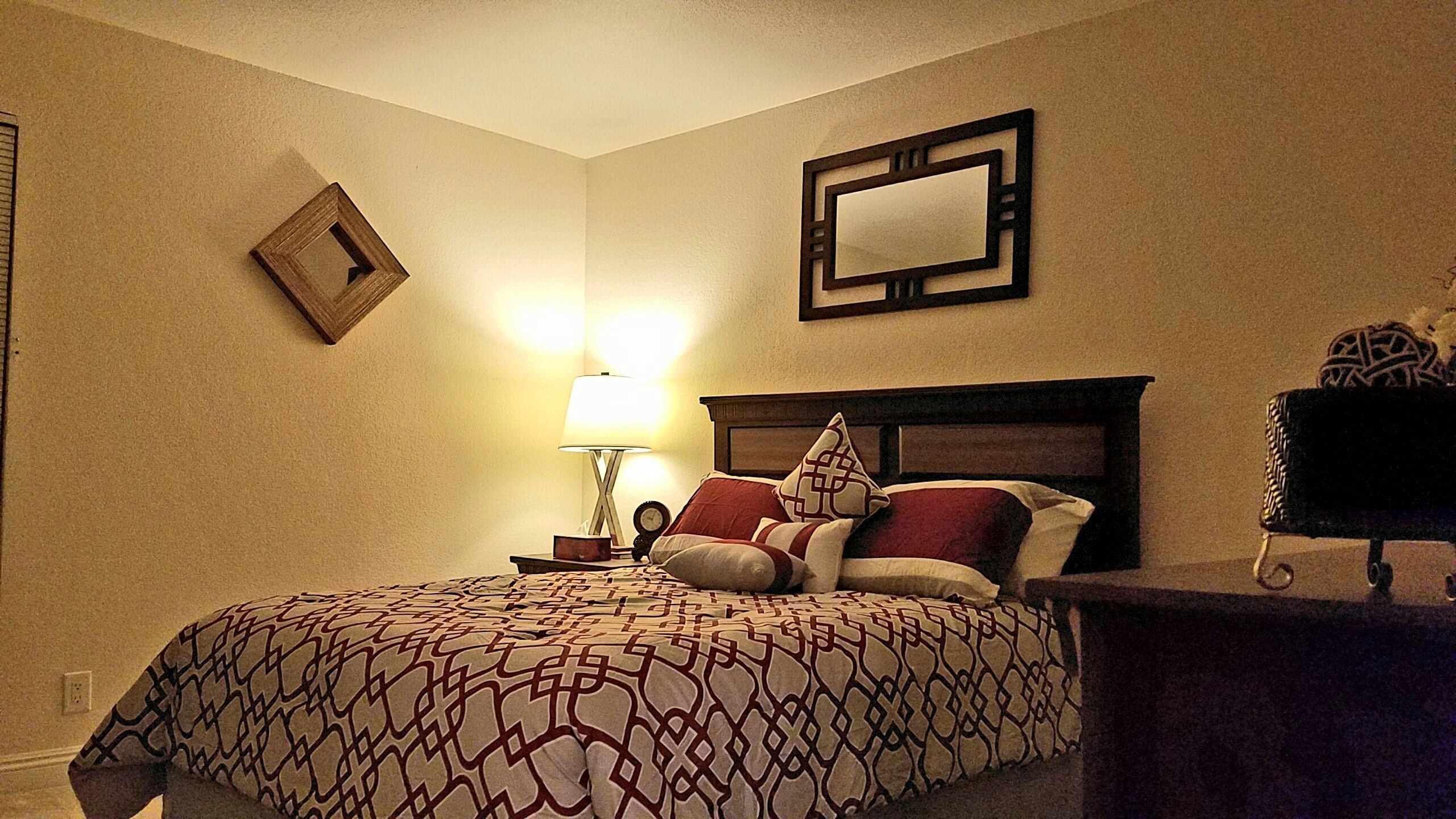 A neatly arranged bedroom with a bed, a bedside table, a lamp, and a mirror on the wall.