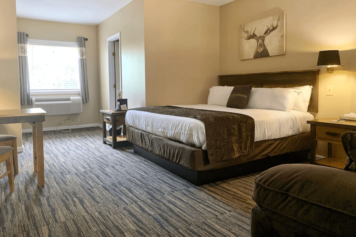 A hotel room with a large bed, a desk, a chair, a window with curtains, and a painting on the wall.