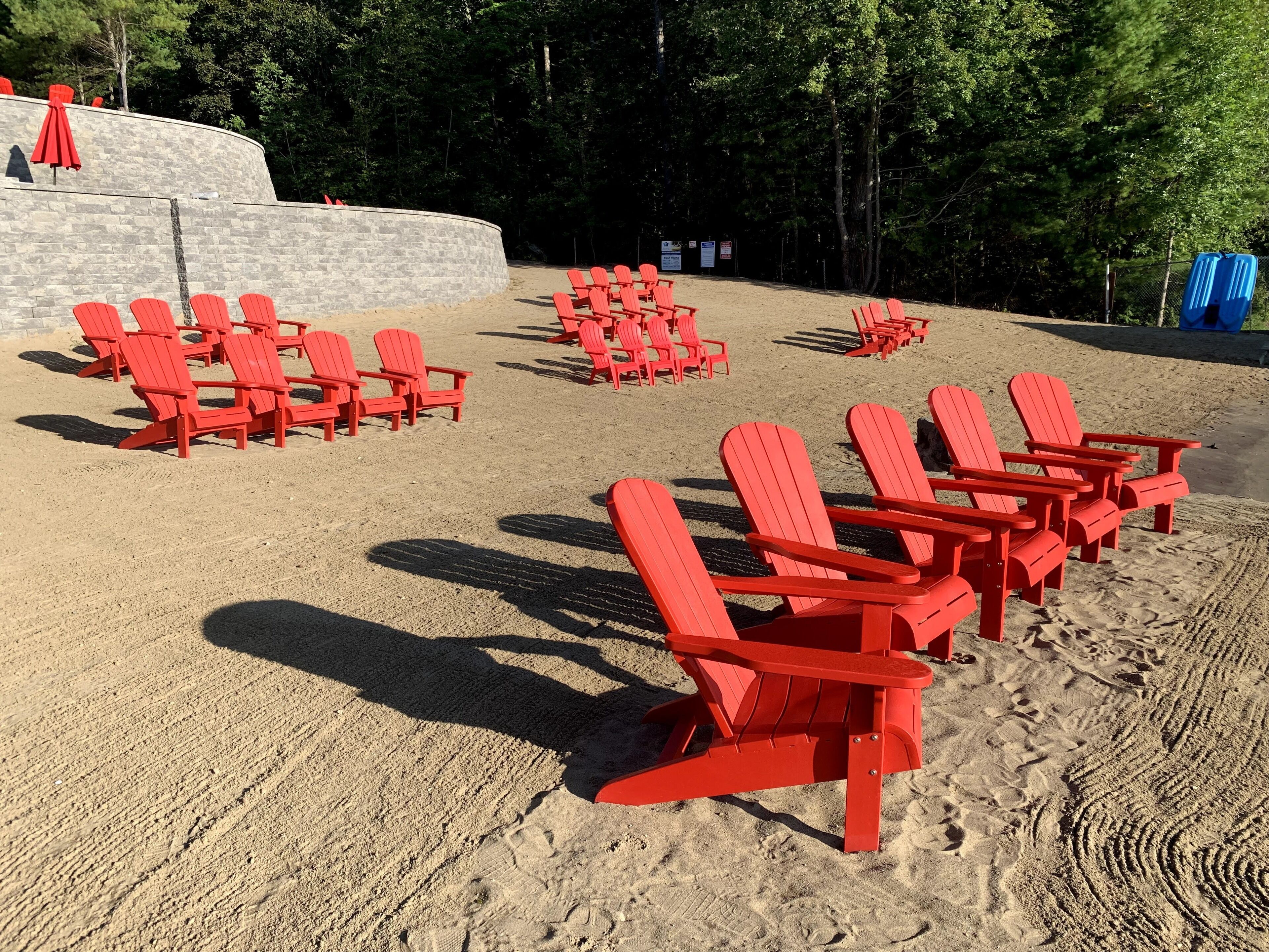 A beach with rows of red Adirondack chairs and a stone wall in the background.