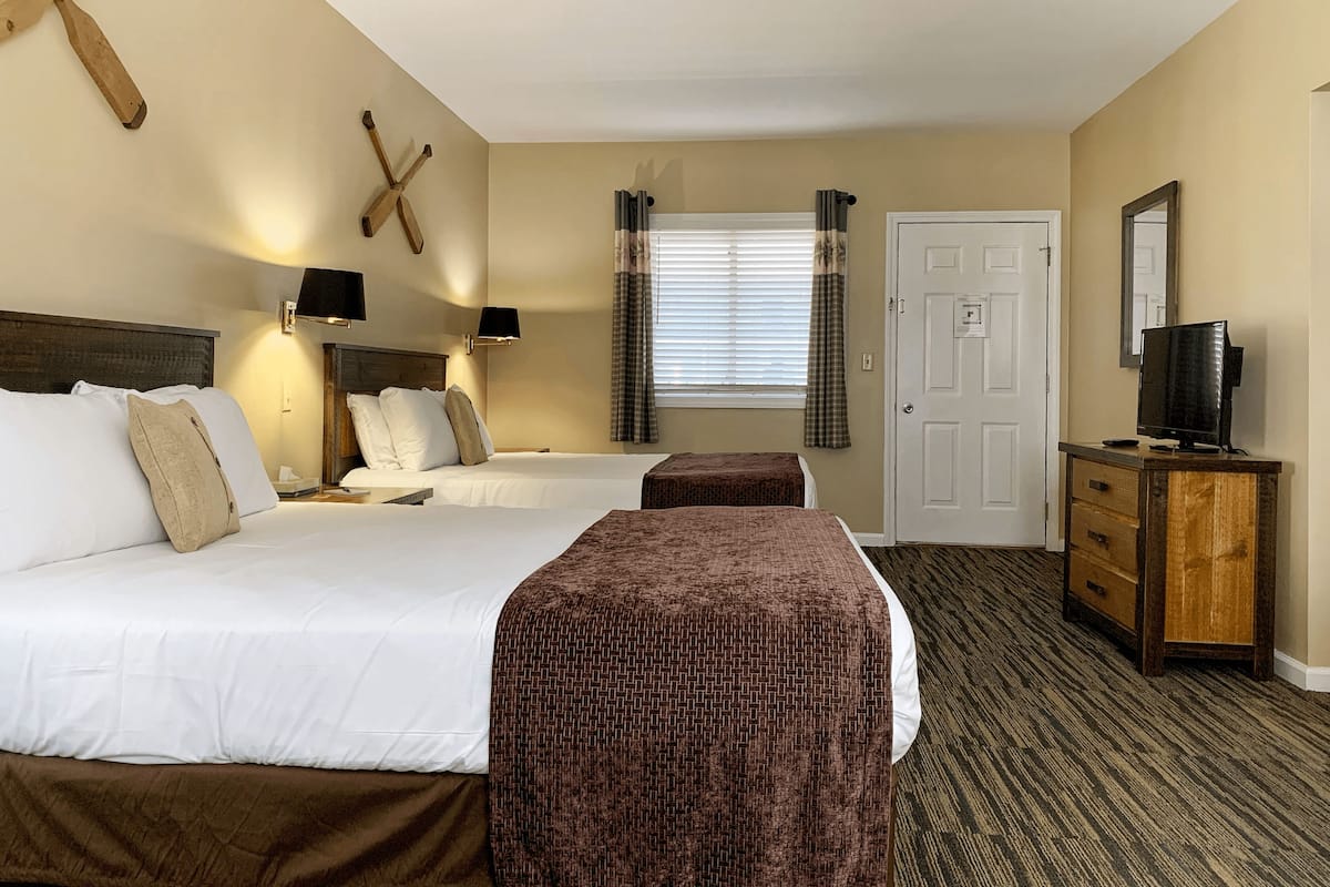 A hotel room with two beds, a wooden headboard, a television on a wooden cabinet, and a window with curtains.
