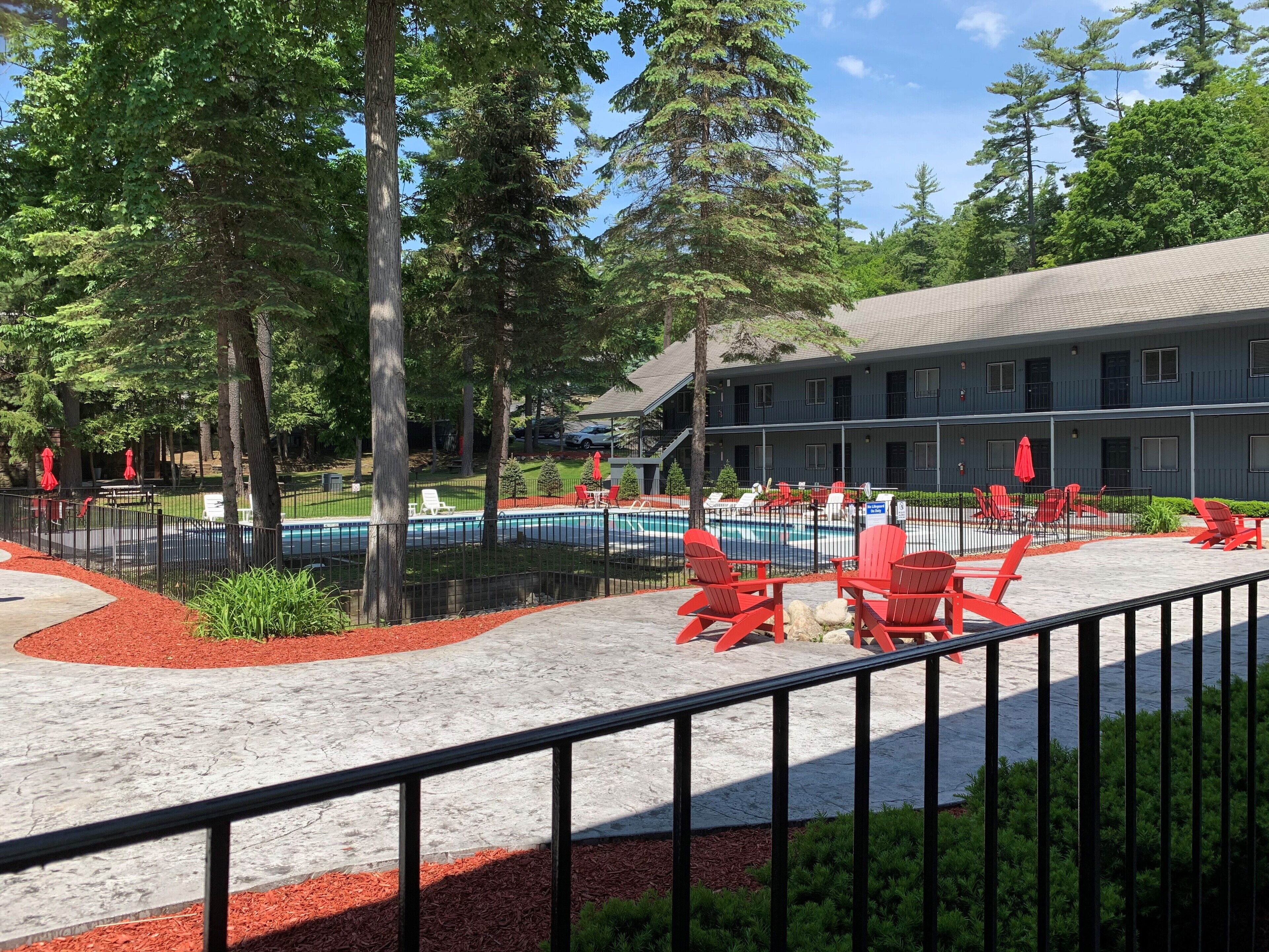 A pool area with red chairs and umbrellas, surrounded by a fence and trees.
