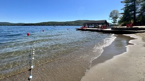 A lakeside view with clear water, a dock, red chairs, and a covered seating area.